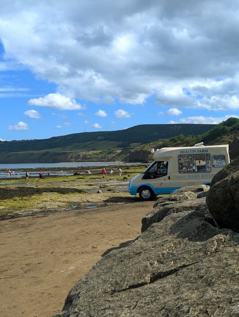 View of Robin Hood’s Bay beach with an ice cream van parked near the shore, capturing seaside charm on the North Yorkshire coast on a sunny summers day.